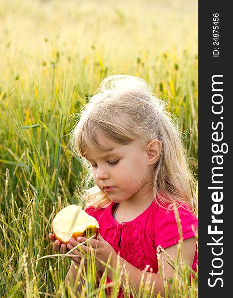 Beautiful serious girl biting an apple in a wheat field. Beautiful serious girl biting an apple in a wheat field