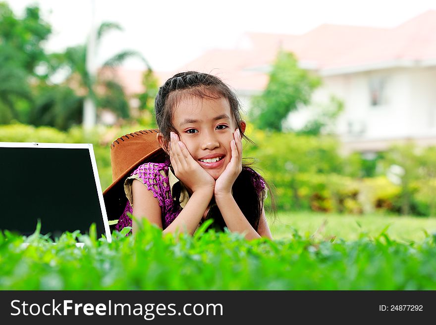 Cute of young girl smiling on the grass with laptop on a holidays