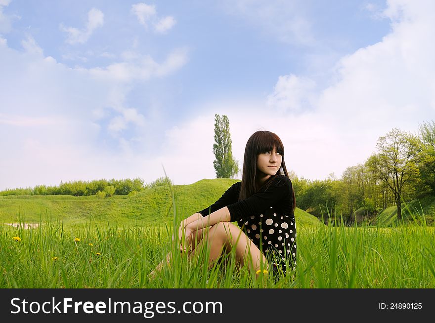 Girl sitting on green grass with blue sky and clouds. Girl sitting on green grass with blue sky and clouds