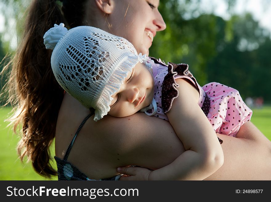 Woman holds child on shoulder in the park