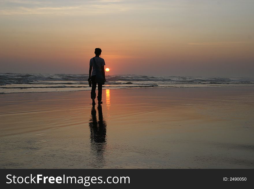 The girl who standing alone in the beach sunset and has reflection in the water. The girl who standing alone in the beach sunset and has reflection in the water