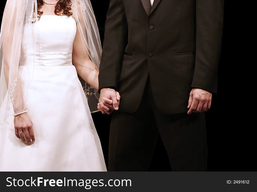 Bride and groom holding hands during their wedding ceremony with bride's engagement ring showing