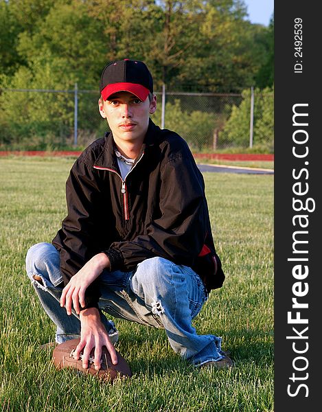 A handsome young boy kneeling on a football field with his football. A handsome young boy kneeling on a football field with his football