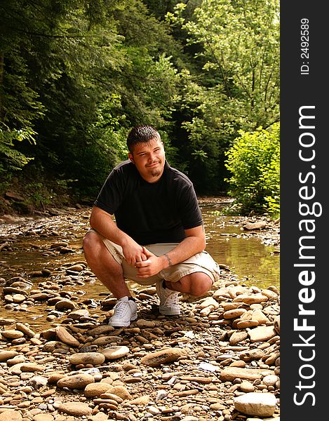 A handsome young man sitting by a creek. A handsome young man sitting by a creek