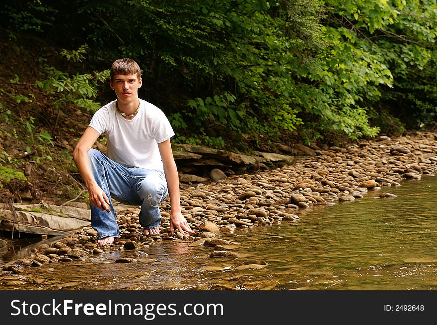 A handsome young teenage boy kneeling by a creek. A handsome young teenage boy kneeling by a creek