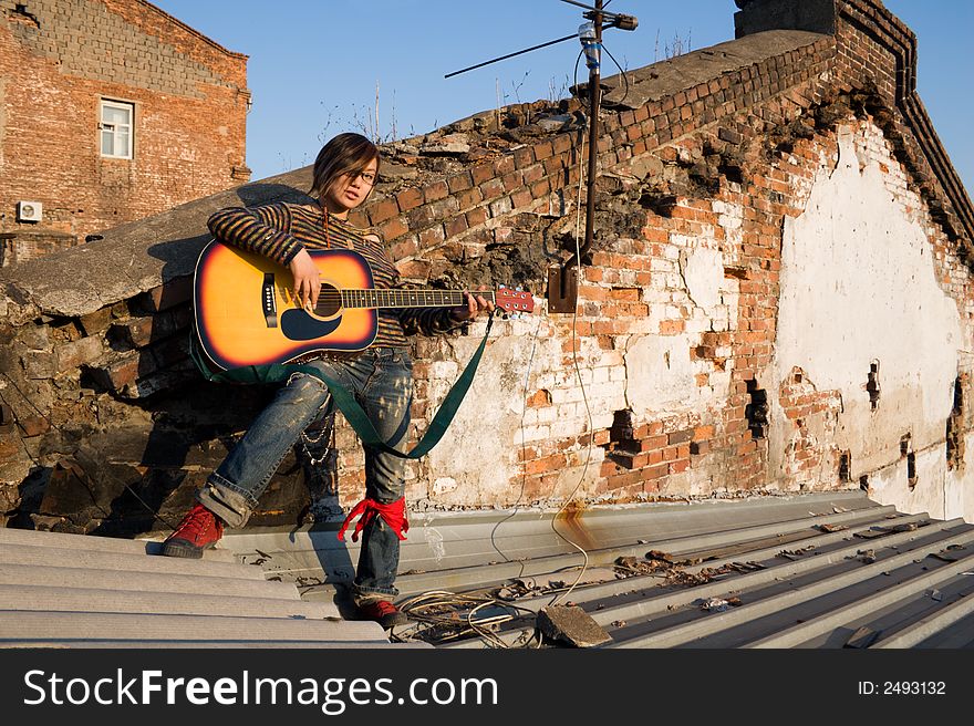 The romantic girl playing beautiful solo on a guitar on the old houses roofs. The romantic girl playing beautiful solo on a guitar on the old houses roofs.