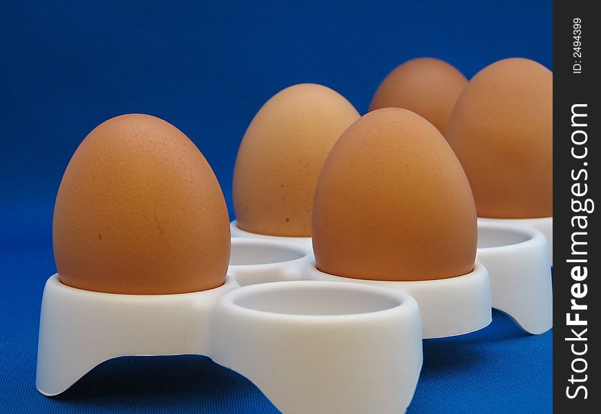 Closeup eggs in a white eggcup on the blue background. Closeup eggs in a white eggcup on the blue background