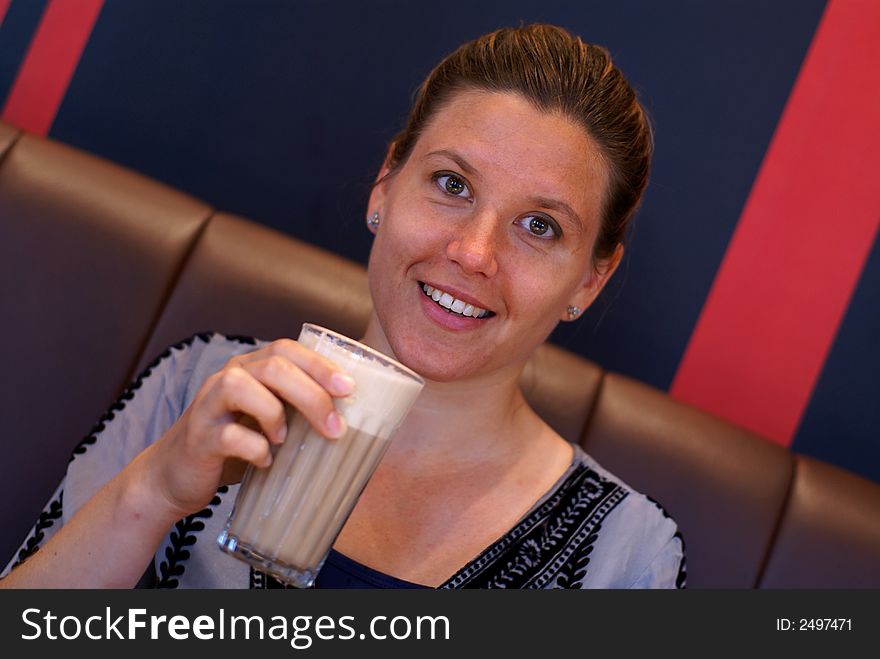 A young woman drinks a warm coffee with foamed milk and smiles at the camera. A young woman drinks a warm coffee with foamed milk and smiles at the camera