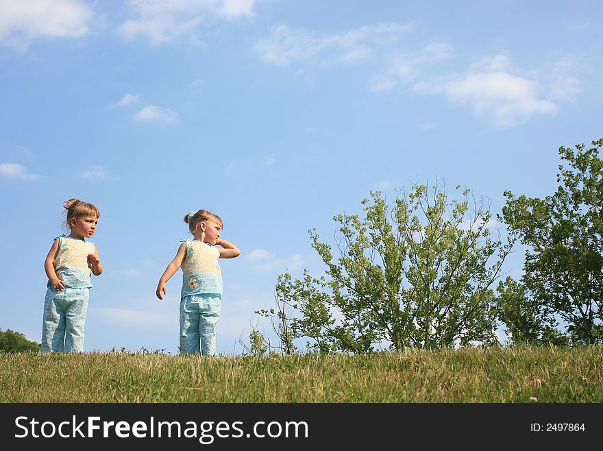 Twin sisters wearing blue against a blue sky with white clouds. Twin sisters wearing blue against a blue sky with white clouds