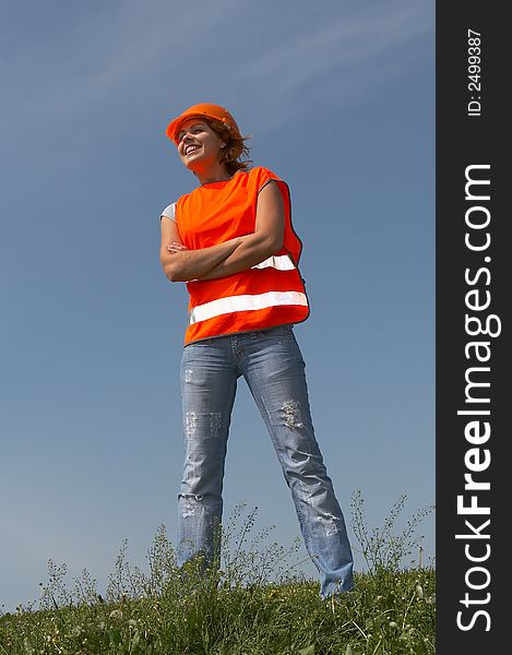 Girl in clothes of the builder worth on a green grass on a background of the blue sky. Girl in clothes of the builder worth on a green grass on a background of the blue sky