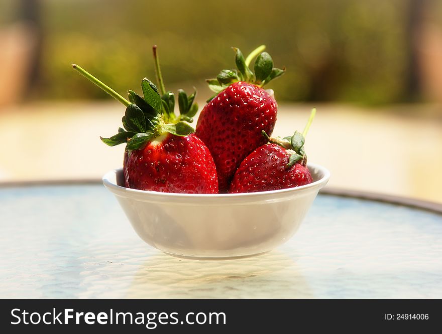 A bowl of large fresh red strawberries photographed over a glass tabletop outdoor. A bowl of large fresh red strawberries photographed over a glass tabletop outdoor