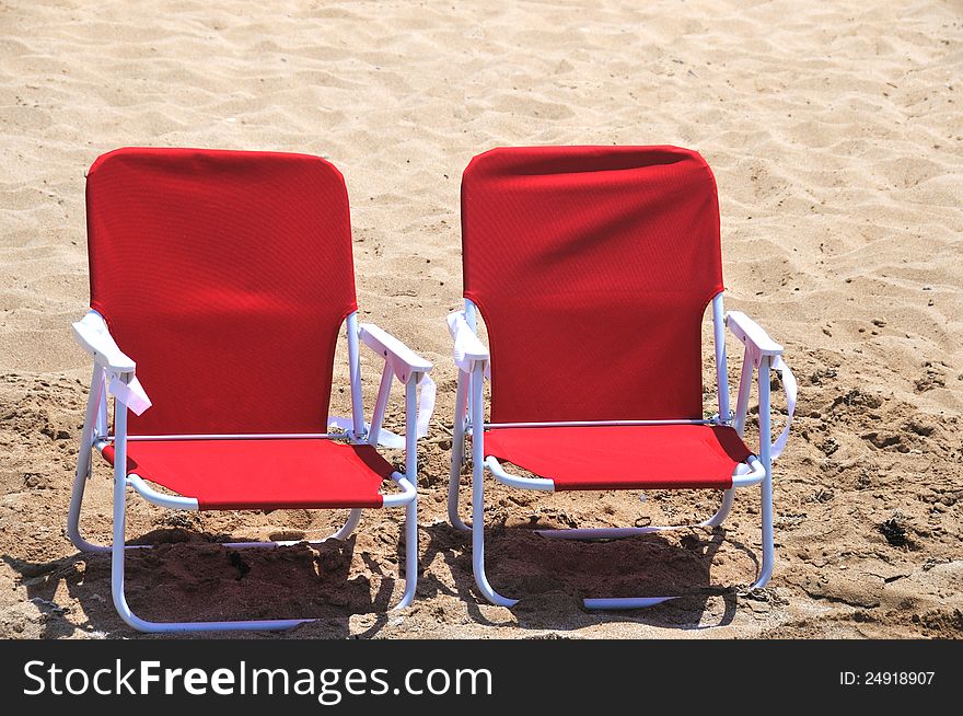 Two red folding beach chairs are in the sand on the beach. Two red folding beach chairs are in the sand on the beach