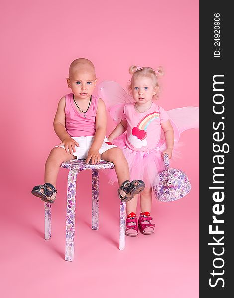 The boy sits on a chair and a girl standing next to a kettle in his hand, on a pink background. The boy sits on a chair and a girl standing next to a kettle in his hand, on a pink background