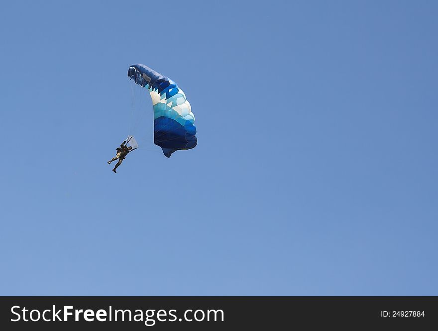 Paratrooper and his blue and white parachute alone against the blue sky