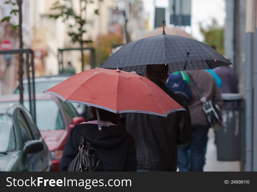 People with umbrellas walking along a street while it is raining. People with umbrellas walking along a street while it is raining