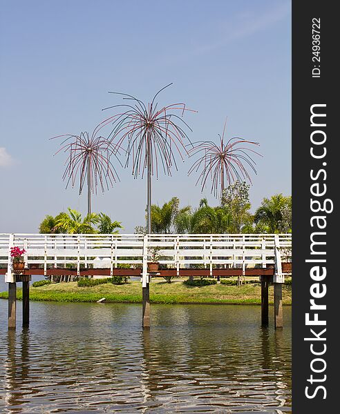 White wooden bridge on the water with poles decorated with coconut trees on a mound. White wooden bridge on the water with poles decorated with coconut trees on a mound.