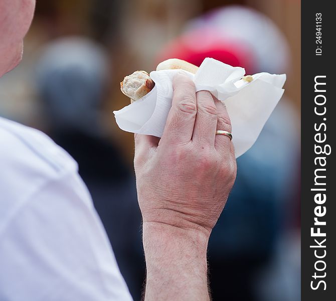 The hand of an unrecognizable man holds a bratwurst with vignette in his hand. A piece of the wurst is already bitten off. The hand of an unrecognizable man holds a bratwurst with vignette in his hand. A piece of the wurst is already bitten off