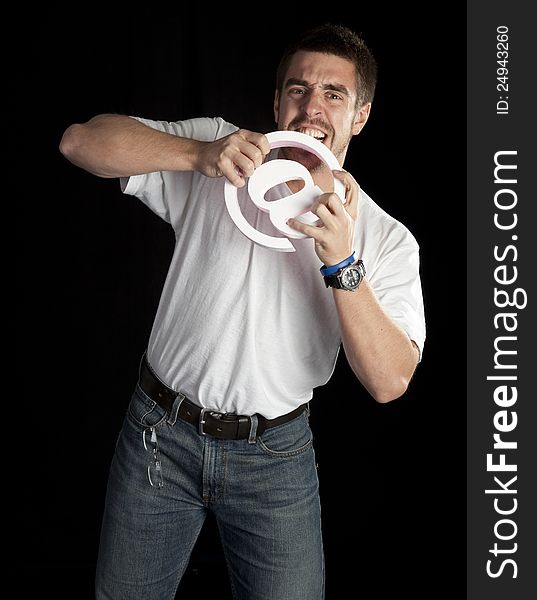 Young angry man bites and email symbol isolated on black in studio. Young angry man bites and email symbol isolated on black in studio