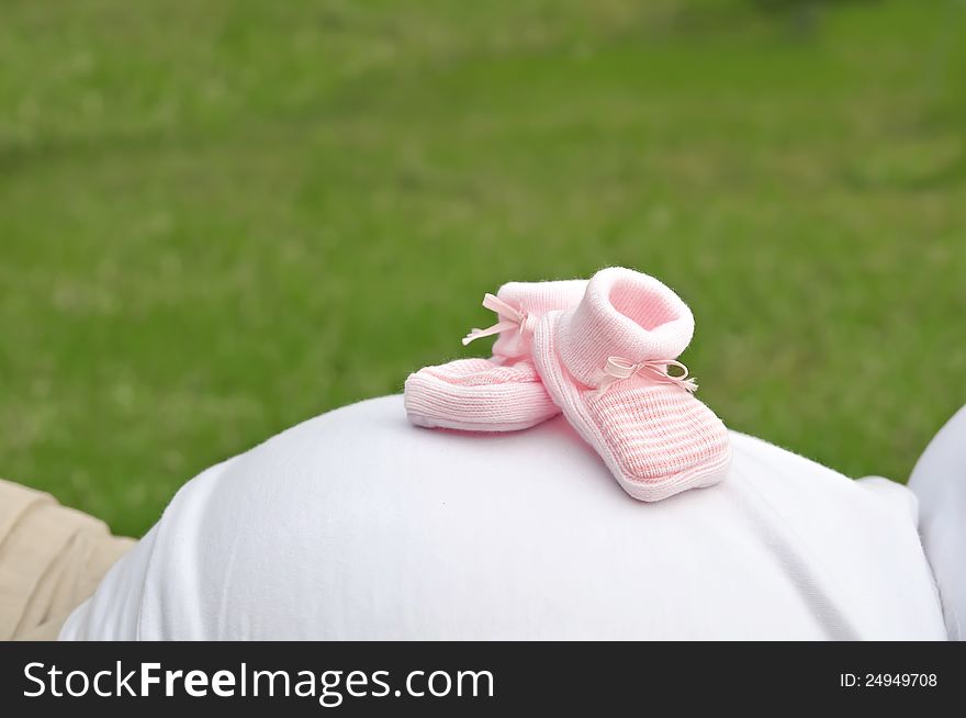 Pink shoes on a pregnant womans belly with a green background. Pink shoes on a pregnant womans belly with a green background