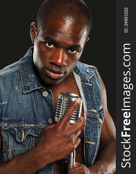 Young African American Singer holding a vintage microphone isolated on a dark background. Young African American Singer holding a vintage microphone isolated on a dark background