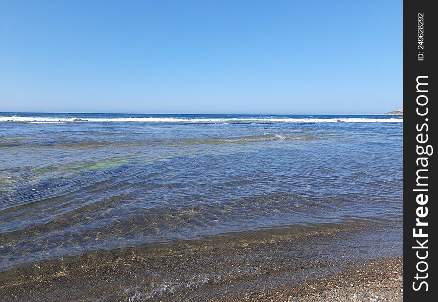 Quiet beach with small transparent waves and black sand. Sunny day at Bejaia, Algeria, North Africa.