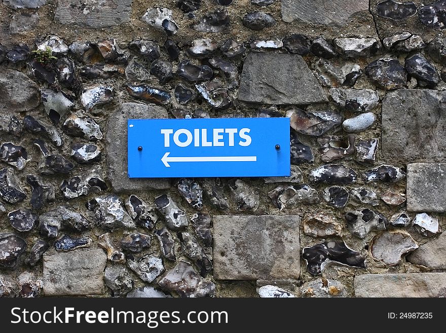 Blue outdoor toilet sign fixed to a flint wall. Blue outdoor toilet sign fixed to a flint wall.