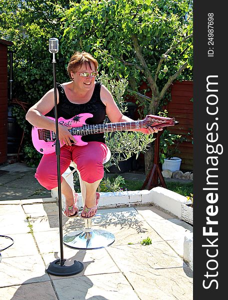 Photo of a woman seated having fun singing and playing a pink inflatable guitar. Photo of a woman seated having fun singing and playing a pink inflatable guitar.