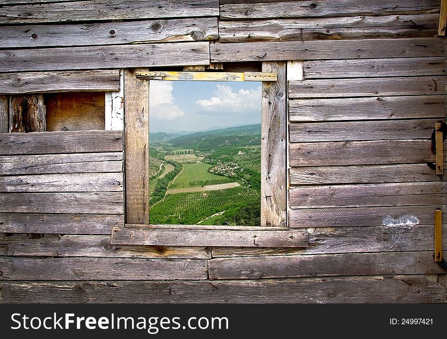 Landscape view through a window frame made in a wooden facade. Old wooden frame on the wall with a farmland view. Countryside with fields in a village - vintage farmhouse background.