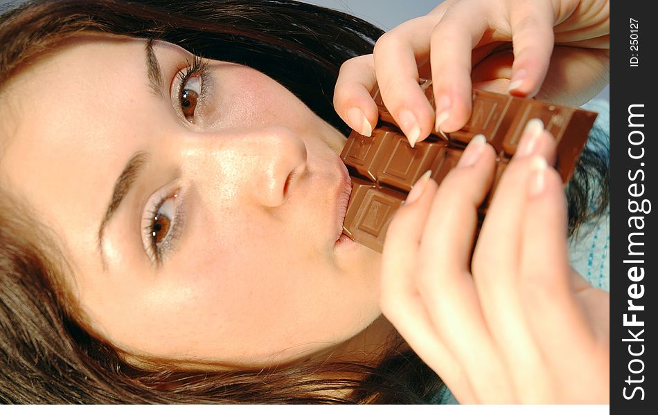 Beautiful girl biting with satisfaction from a chocolate bar. Beautiful girl biting with satisfaction from a chocolate bar