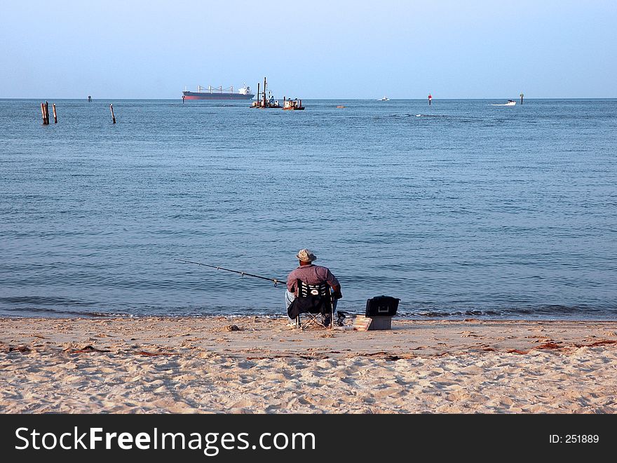 A man and his fishing pole relaxing on the beach. A man and his fishing pole relaxing on the beach.