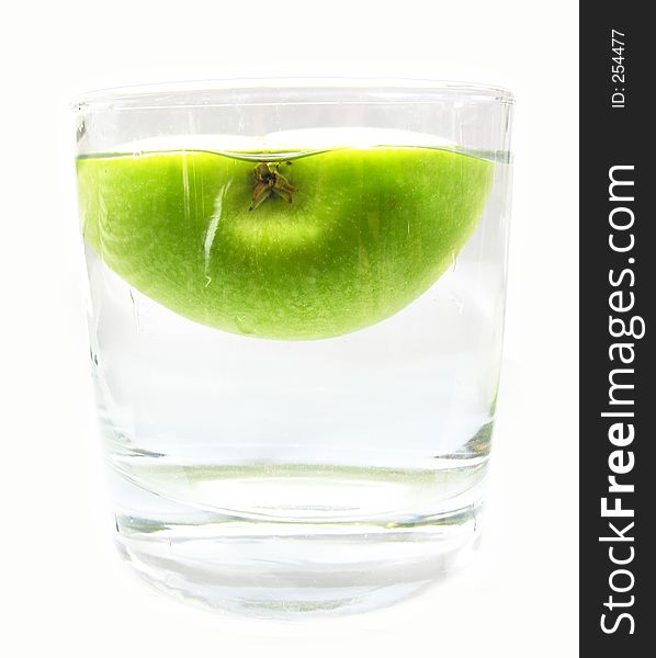 Half a green apple floating in a glass of water. Half a green apple floating in a glass of water