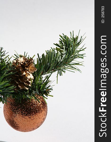 Bronze bauble hanging on greenery sprig with gold fir cone
