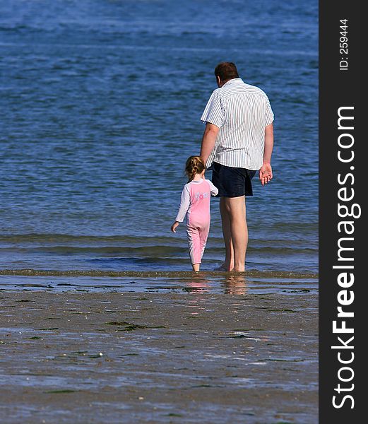 A father holding the hand of his daughter at the beach, whilst paddling together. A father holding the hand of his daughter at the beach, whilst paddling together.