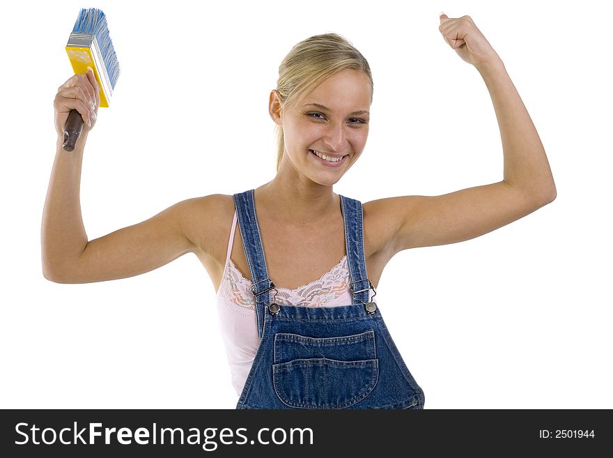Young smiling blonde wearing dungarees with paintbrush in hand. Showing her satisfaction by hands up. Isolated on white in studio. looking at camera. Young smiling blonde wearing dungarees with paintbrush in hand. Showing her satisfaction by hands up. Isolated on white in studio. looking at camera.