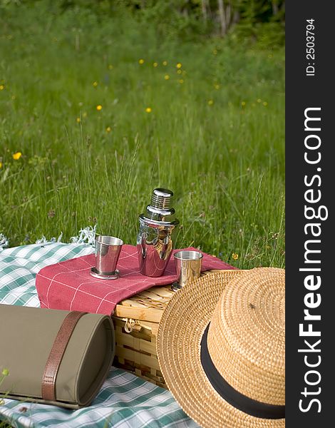 Basket of picnic in grass posed on a tablecloth with a hat