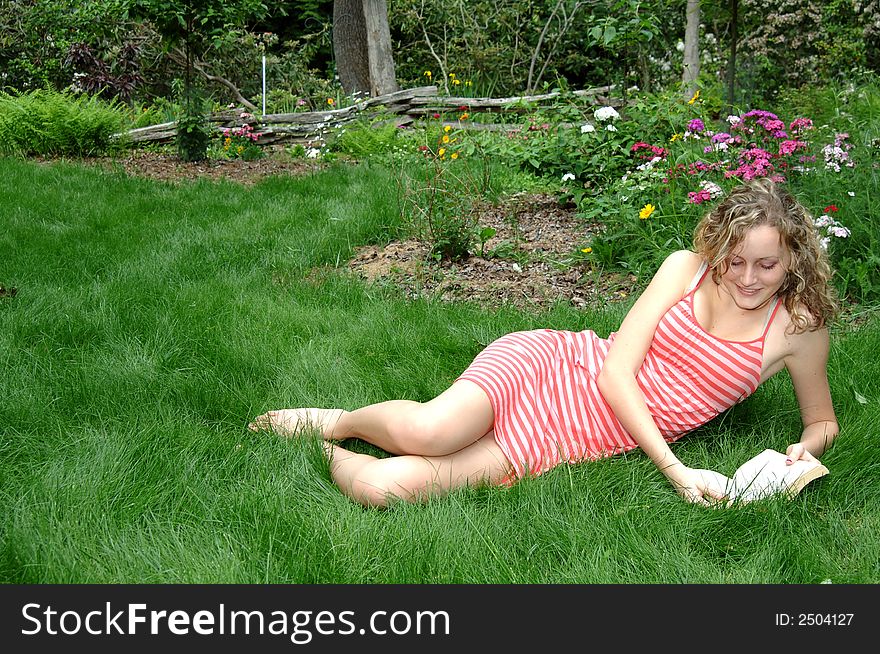 A young woman reading a book on soft grass near flowers. A young woman reading a book on soft grass near flowers