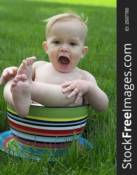 Image of an adorable baby sitting in a colorful, over-sized teacup in the grass. Image of an adorable baby sitting in a colorful, over-sized teacup in the grass