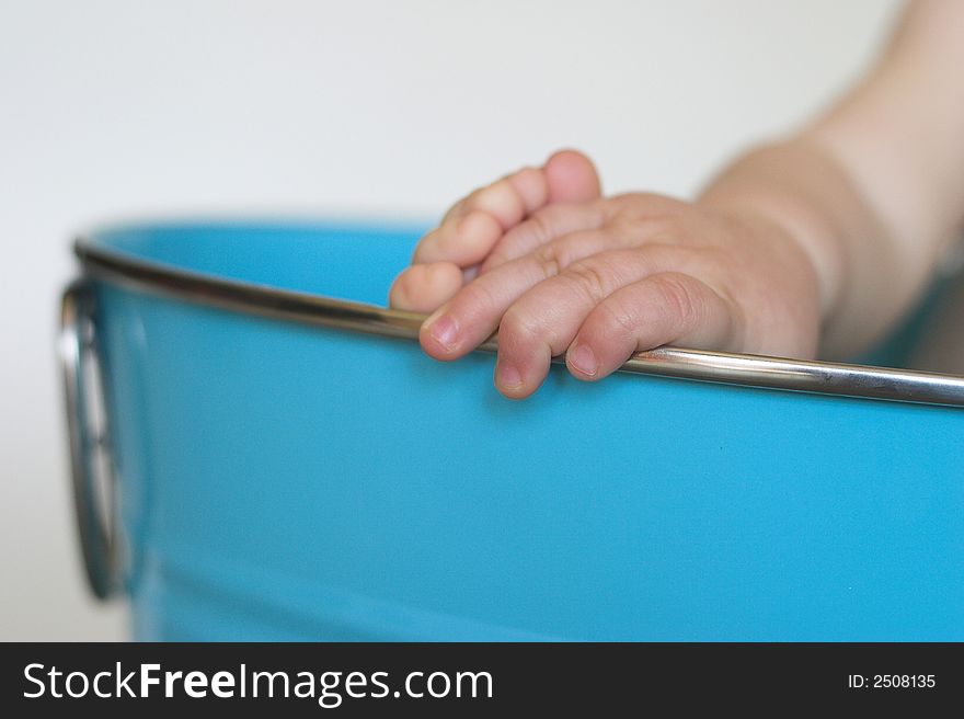 Image of a baby's hand and foot peeking out over the side of a blue tub. Image of a baby's hand and foot peeking out over the side of a blue tub