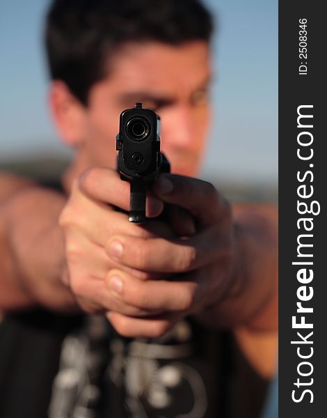 A man holding a pistol and pointing it at the camera. (This image is part of a series). A man holding a pistol and pointing it at the camera. (This image is part of a series).