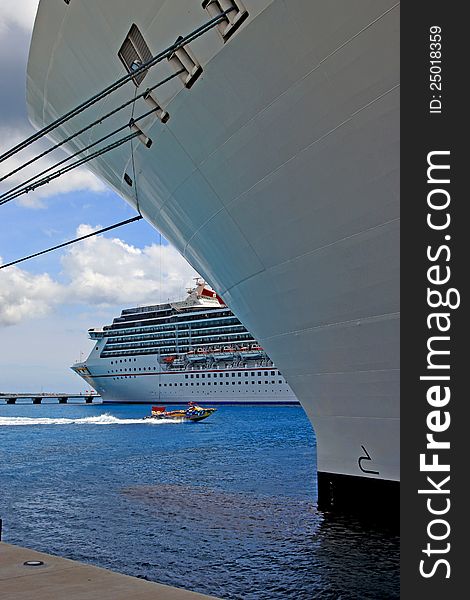 Two cruise line ships in port, one docked the other anchored.