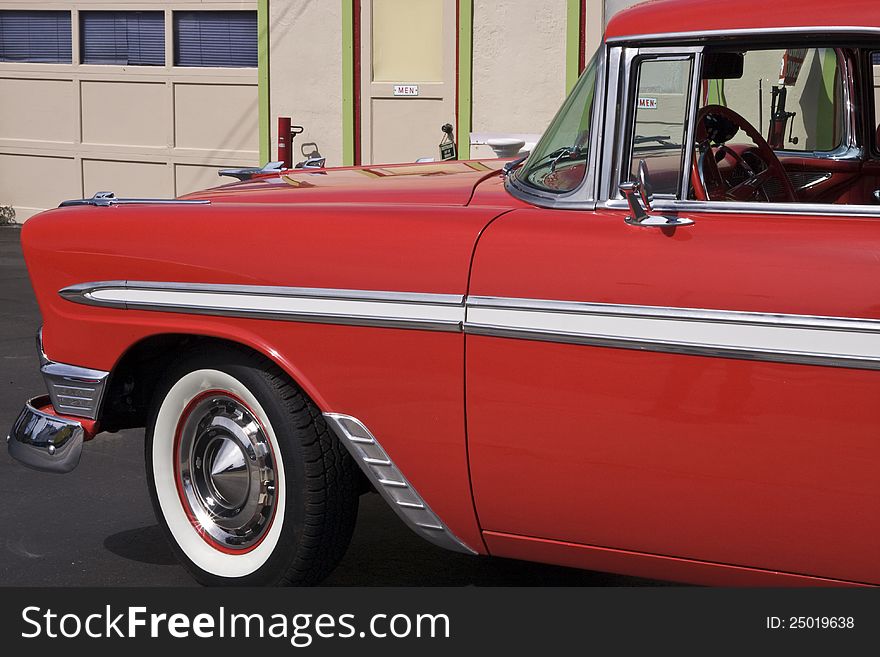 An old classic show car painted red at a historic gas station with a nice hood ornament. An old classic show car painted red at a historic gas station with a nice hood ornament