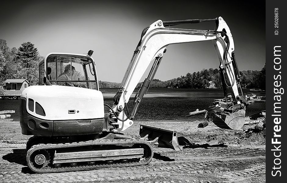 A man doing construction work in a backhoe on a beach in black & white. A man doing construction work in a backhoe on a beach in black & white.