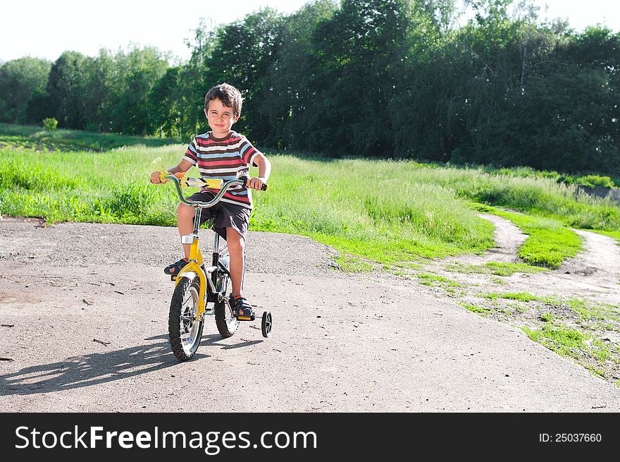 Little boy riding bike on country road outdoors in sunny day