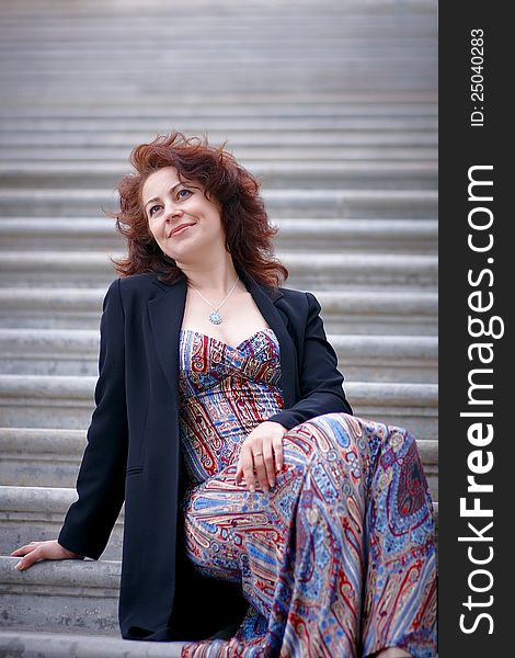 Portrait of the beautiful dreaming woman in a jacket sitting on steps