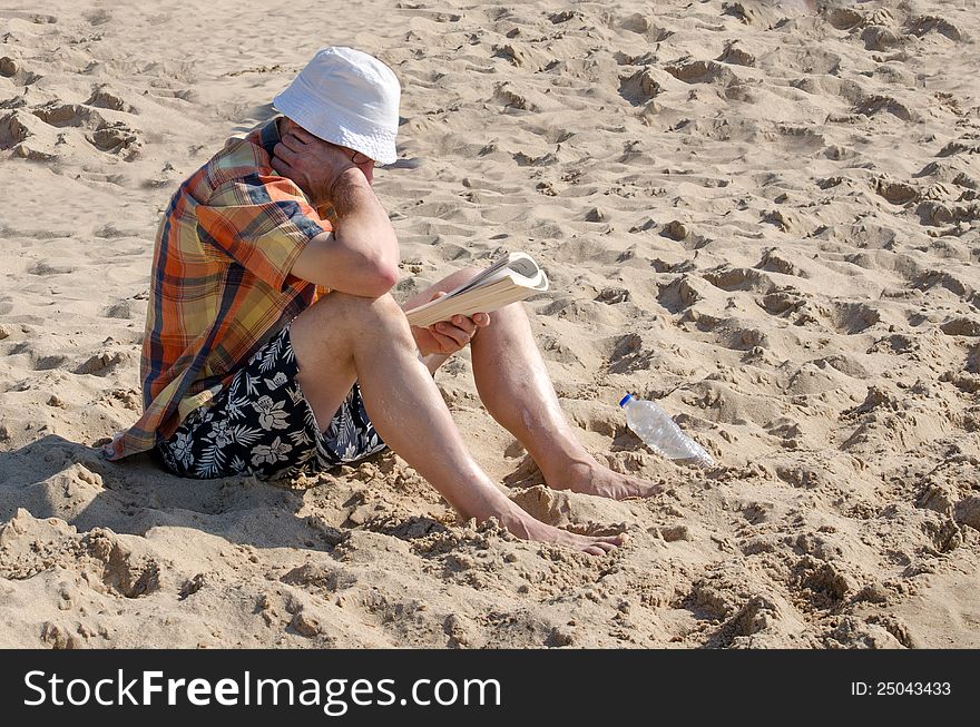 A man sits on the beach reading a magazine and keeping covered up from the hot sun. A man sits on the beach reading a magazine and keeping covered up from the hot sun