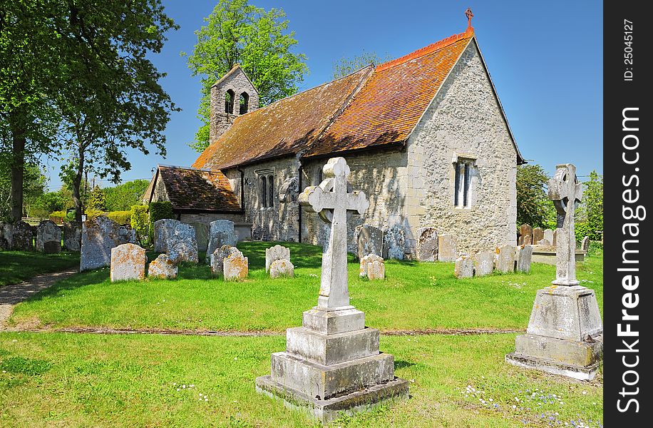 English Village Church viewed from the graveyard with stone cross in the foreground. English Village Church viewed from the graveyard with stone cross in the foreground