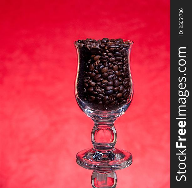 Grains of black roasted coffee in transparent cup  on red background. Grains of black roasted coffee in transparent cup  on red background