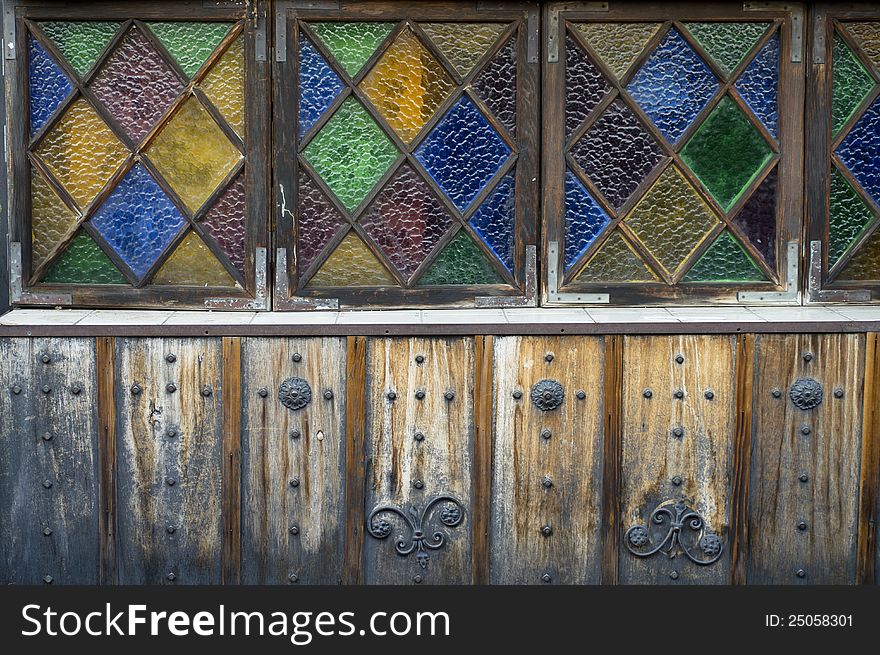 Colored glass windows on an old wood-sided building with iron studs and decoration. Colored glass windows on an old wood-sided building with iron studs and decoration.