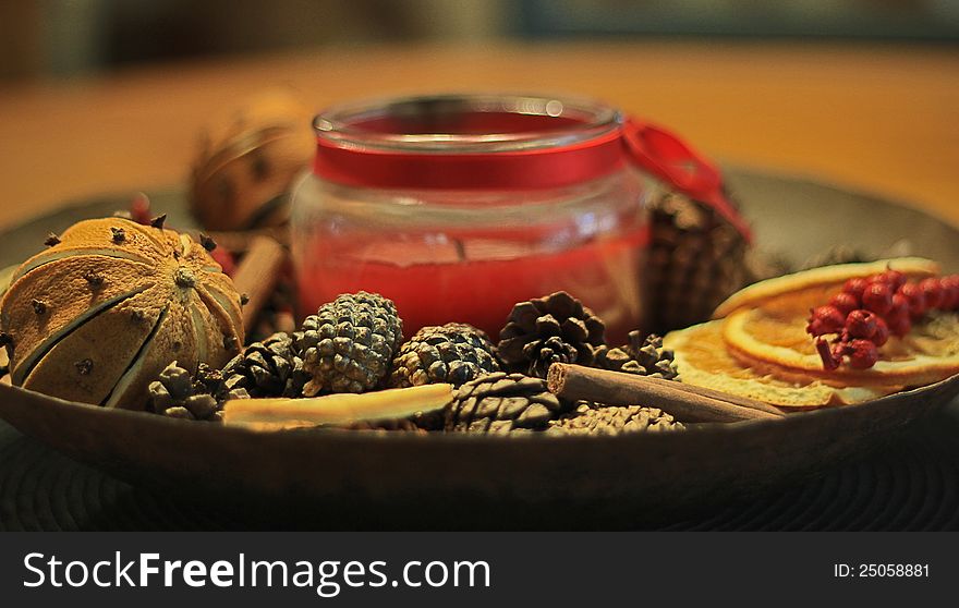 Potpourri bowl including orange and cloves, pine cones, berries, cinnamon, and a candle.