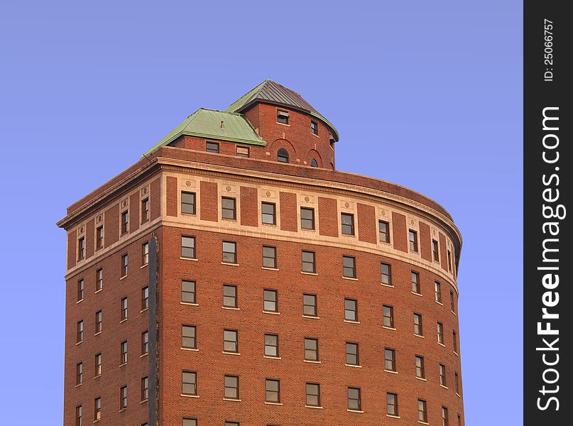 Upper stories of an old red brick building with a curved front and windows, isolated against the blue sky. Upper stories of an old red brick building with a curved front and windows, isolated against the blue sky.